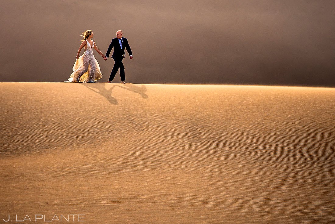 bride and groom walking along sand dunes