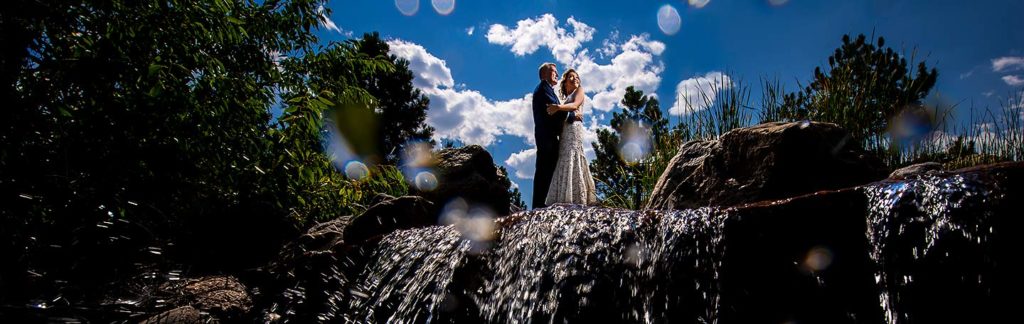 portrait of bride and groom standing on top of waterfall