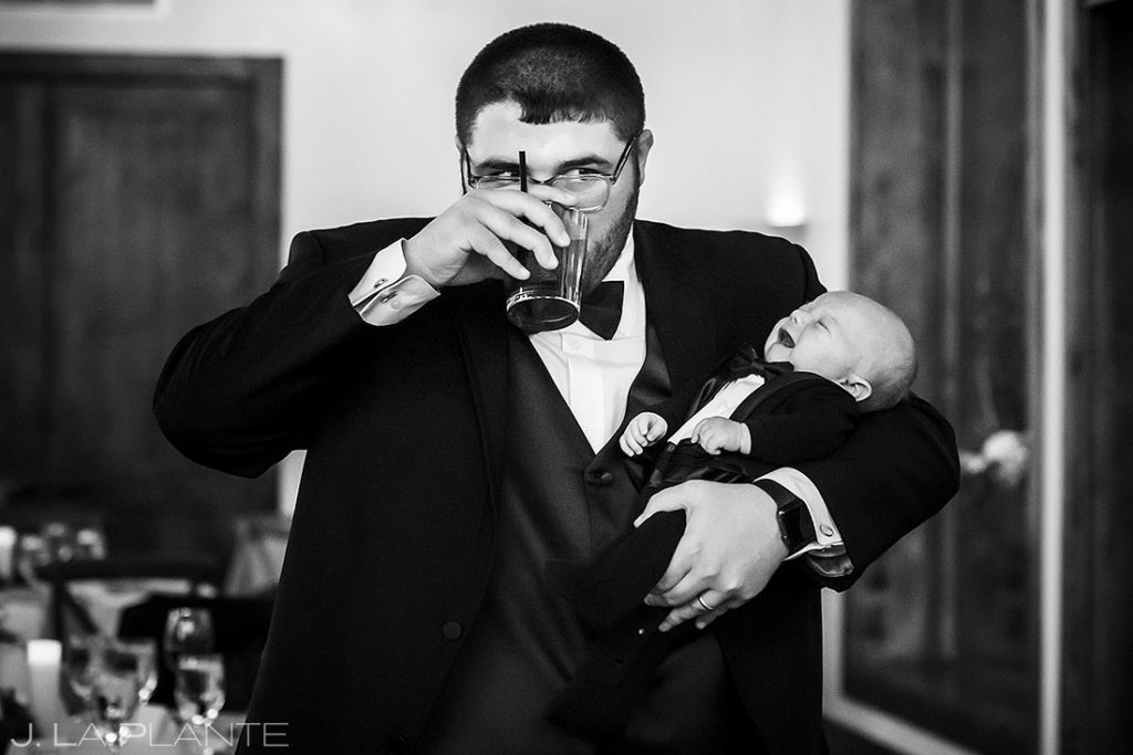 wedding guest holding crying baby while taking a drink