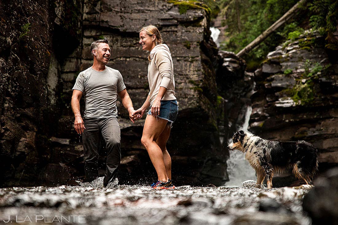 bride and groom playing with dog under mountain waterfall