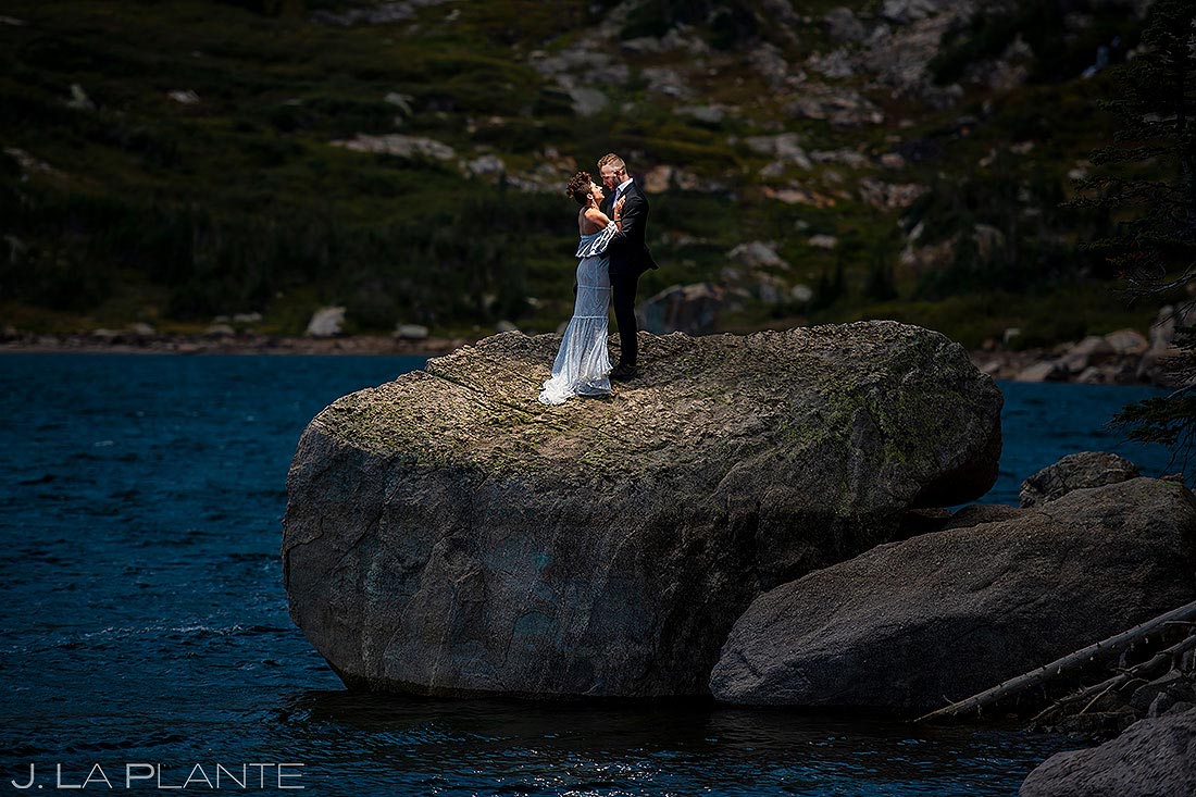 bride and groom kissing on rock in mountain lake