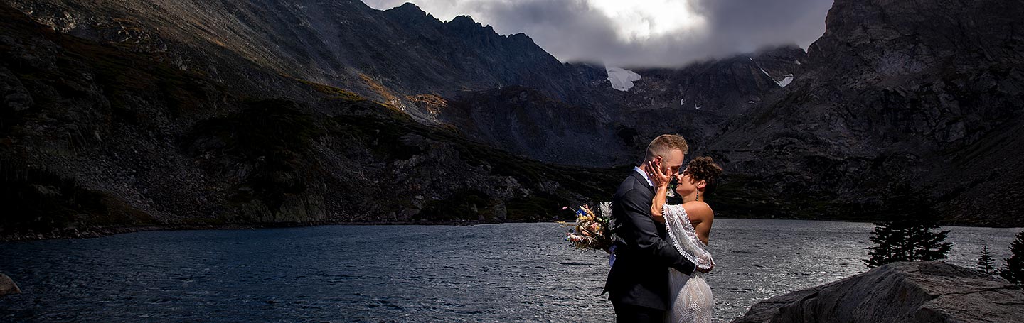 bride and groom kissing at mountain lake