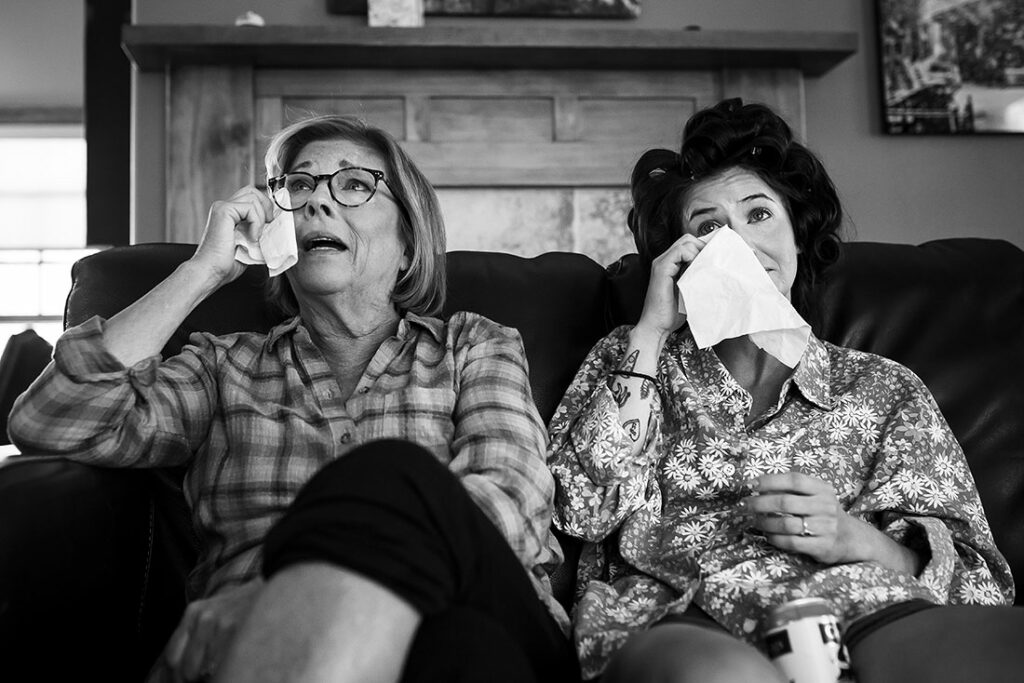 bride crying with her mother while watching photo slideshow